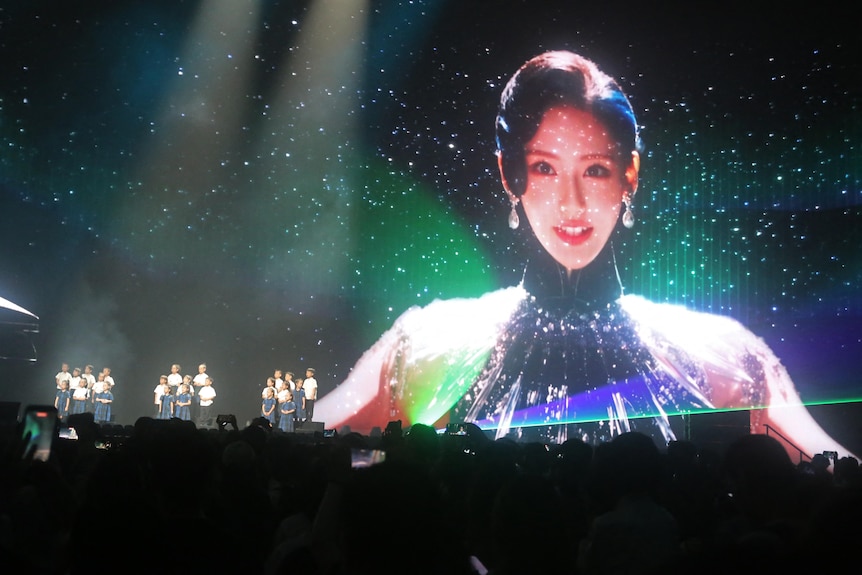 Yuri shown as a woman in a black dress on a large stage screen during a live concert
